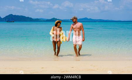 Ein vielfältiges Paar Männer und Frauen, die vom Meer zum Strand von Koh Kradan Island Thailand laufen, kaukasische Männer und asiatische Frauen im Sommerurlaub, die durch Thailand reisen Stockfoto