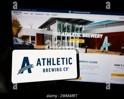 Person mit Smartphone und Logo des US-amerikanischen Getränkeherstellers Athletic Brewing Company vor der Website. Schwerpunkt auf dem Display des Telefons. Stockfoto