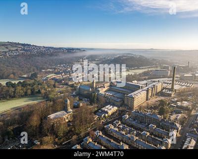 Blick aus der Vogelperspektive auf das Dorf Saltaire und die Salts Mill, die zum UNESCO-Weltkulturerbe in West Yorkshire gehören. Kaltes und frostiges Wetter mit hellem, sonnigem Himmel und anhaltendem Nebel. Stockfoto