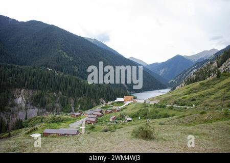 Traditionelles Kasachstans Jurtencamp im malerischen Bergtal in der Nähe des Flusses. Gemütliche Filz- und Holzjurten bieten lokale Gastfreundschaft inmitten von schneebedeckten Gipfeln. Stockfoto