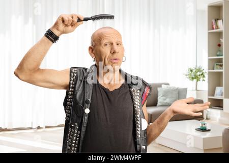 Ein verwirrter Mann, der zu Hause eine Haarbürste über seinem Glatzkopf hält Stockfoto