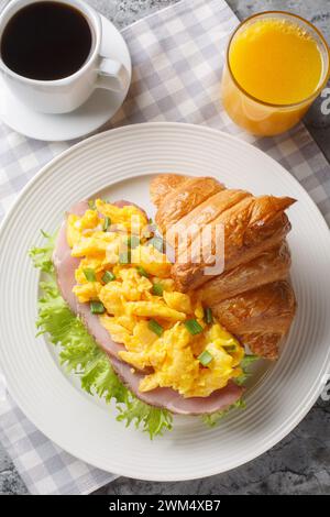 Croissant-Sandwich mit Omelette, Schinken und Salat, serviert mit Orangensaft und Kaffee aus nächster Nähe auf einem Marmortisch. Vertikale Draufsicht von oben Stockfoto