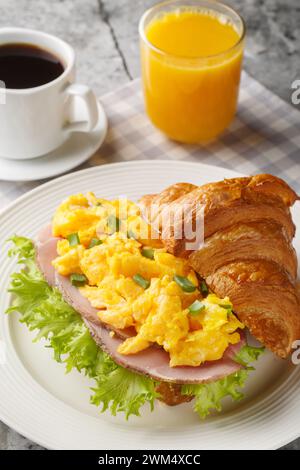 Rührei, Schinkencroissant, serviert mit Orangensaft und Kaffee aus nächster Nähe auf einem Marmortisch. Vertikal Stockfoto