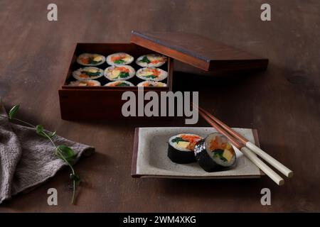 Kimbap in einer Holzkiste mit Stäbchen auf hölzernem Hintergrund Stockfoto