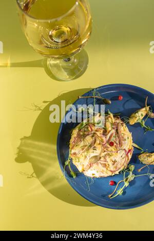 Salat mit Meeresfrüchten mit saftigen Garnelen, Krabben, Avocado und leichter Mayo auf einem blauen Teller. Serviert mit Weißwein auf gelbem Hintergrund. Perfekt für ein Licht Stockfoto