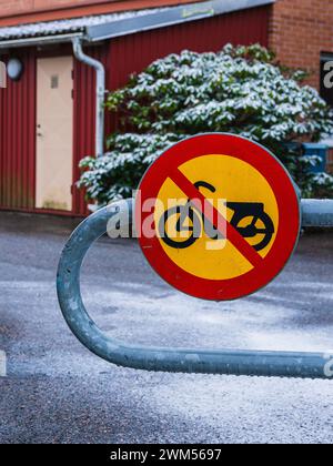 Ein hellrotes und gelbes Schild mit dem Hinweis „keine Motorräder erlaubt“ ist vor dem Hintergrund von leichtem Schneefall deutlich sichtbar zu sehen. Die Szene fängt eine ruhige, winterliche Atmosphäre ein Stockfoto