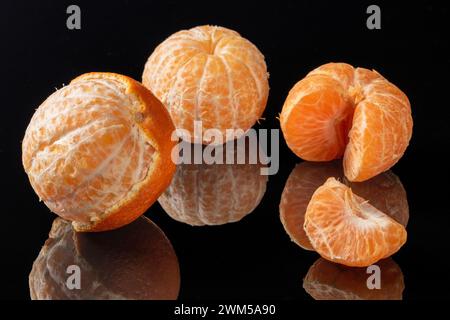 Drei lebendige und saftige Mandarinen, geschält und auf einer reflektierenden Oberfläche angeordnet, schaffen einen faszinierenden Spiegeleffekt mit einem wunderschönen Spiel von Li Stockfoto