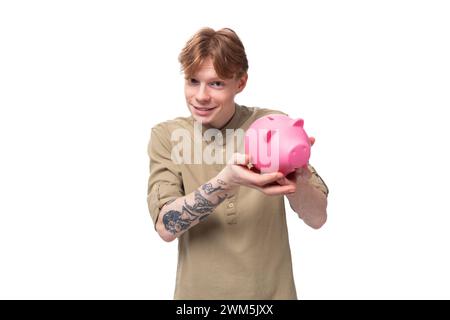 Junger rothaariger Kerl in Brille und braunem Hemd hält eine rosa Schweinebank Stockfoto