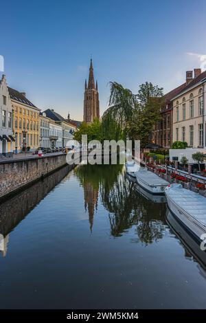 Abendliche Atmosphäre auf einem Kanal in der Altstadt von Brügge. Alte Gebäude und Boote entlang des Wassers mit einer Straße. Im Hintergrund steht die Kirche Stockfoto