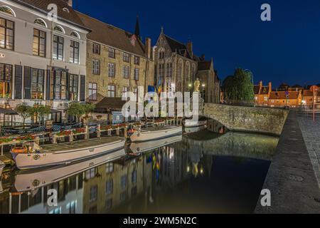 Beleuchtete Häuser am Kanal in Brügge am Abend. Hansestadt in Belgien zur blauen Stunde. Historische Kaufmannshäuser in der Hansestadt. Stockfoto