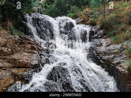 Kleiner Wasserfall mit Wasser, das über braune Steine fließt. Natürliche Landschaft mit malerischem Wasserfall, der über rauen braunen Felsen fließt Stockfoto