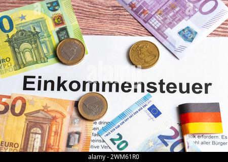 Augsburg, Bayern, Deutschland - 24. Februar 2024: Euro-Banknoten mit einem Dokument mit der Aufschrift Einkommensteuer *** Euro Geldscheine mit einem Dokument mit Aufschrift: Einkommensteuer Stockfoto