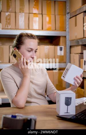 Frau, die ein Mobiltelefon oder Tablet verwendet, um mit Kunden zu kommunizieren. Lieferung von Waren über private Kurierdienste. Konzepte des Online-Verkaufs und weiter Stockfoto