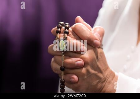 Reife Frau betet den Rosenkranz vor einem violetten Hintergrund. Stockfoto