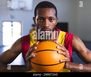 Fokussierter afroamerikanischer Mann, der einen Basketball in einem Fitnessstudio hält Stockfoto