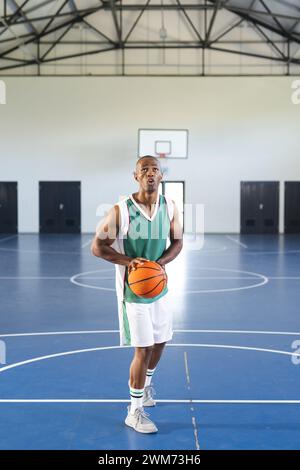 Afroamerikaner macht sich bereit, in einem Fitnessstudio mit Kopierraum einen Basketball zu schießen Stockfoto