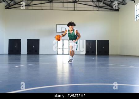 Ein junger birassischer Mann dribbelt einen Basketball auf einem Hallenplatz mit Kopierraum Stockfoto