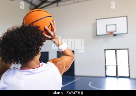 Ein junger birassischer Mann bereitet sich darauf vor, einen Basketball in einer Halle mit Kopierraum zu schießen Stockfoto