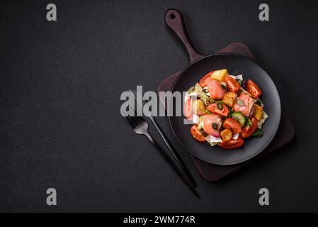 Köstlicher saftiger Salat mit Lachs, Tomaten, Gurke, Kräutern, Kürbiskernen, Salz und Gewürze in einer Keramikplatte auf dunklem Betonhintergrund Stockfoto