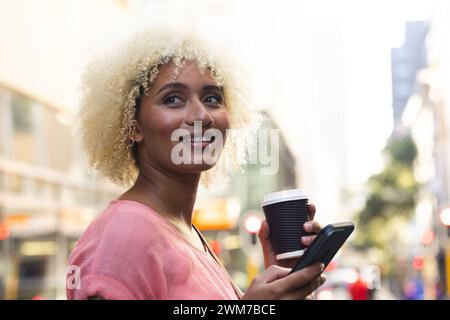 Eine junge Frau, die eine Rasse hat, genießt einen Kaffee im Freien in der Stadt Stockfoto