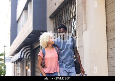 Ein junges, vielseitiges birassisches Paar spaziert zusammen im Freien und trägt Gepäck im Urlaub Stockfoto