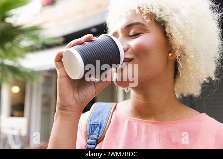 Eine junge Frau, die eine Rasse hat, genießt einen Kaffee im Freien in der Stadt Stockfoto