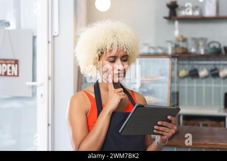 Eine junge Barista, weibliche Café-Besitzerin, untersucht ein Tablet in einem Café Stockfoto