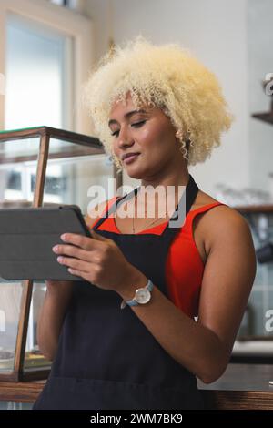 Die junge Barista, weibliche Biracial Café-Besitzerin, überprüft ein digitales Tablet in einem Café Stockfoto