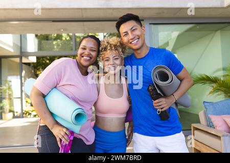Ein junger asiatischer Mann und zwei junge Frauen posieren draußen mit Yogamatten Stockfoto
