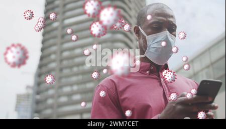 COVID-19-Zellen schweben gegen afroamerikaner, der eine Gesichtsmaske mit Smartphone trägt Stockfoto