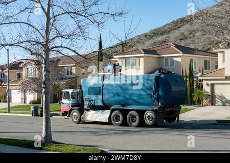 Ein blauer Müllwagen sammelt Müll aus großen Mülltonnen an der Seite einer Wohnstraße Stockfoto