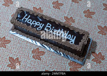 Feierliche Freude. Schokoladenkuchen mit Happy Birthday weißen Buchstaben. Herbstmotiv, Blatttabelle. Stockfoto