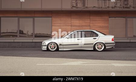 BMW 3er Limousine (E36) parkt vor einem modernen Gebäude. Youngtimer Low Car in der Stadt an einem sonnigen Tag. Stockfoto