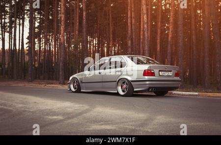 Silver BMW 3er Limousine (E36) parkt in der Nähe von Kiefernhainen. Blick auf den Youngtimer Low Car auf dem Land. Stockfoto