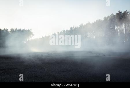 Parkplatz im Nebel. Rauchnebel nach dem Driften und Kiefernwald im Hintergrund. Stockfoto