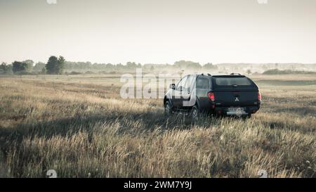 Schwarzer Mitsubishi SUV-Pickup-Truck auf einer Wiese. Morgenlicht um 6:00 Uhr, Dreiviertelansicht hinten. Stockfoto