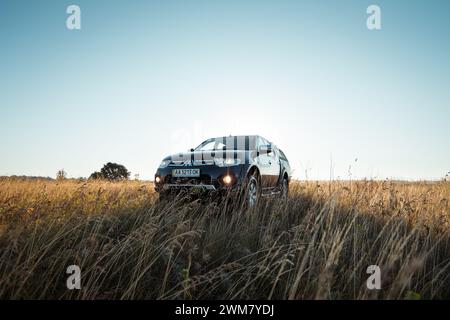 Schwarzer Mitsubishi SUV-Pickup-Truck auf einer Wiese. Morgenlicht um 6:00 Uhr, Dreiviertelblick. Stockfoto