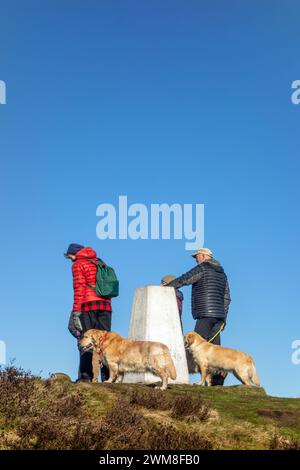 Menschen, die Hunde laufen, hielten an, um zu reden und die Aussicht vom Trig Point auf Eyam Moor über dem Dorf Eyam im Derbyshire Peak District zu genießen Stockfoto