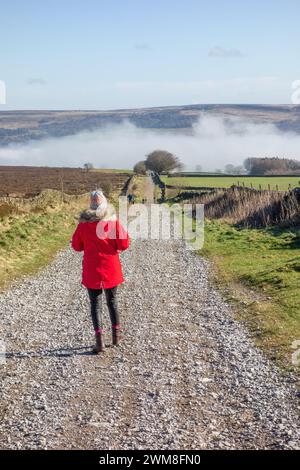 Frau im roten Mantel, die entlang der Sir William Hill Road läuft, einer alten Packhorse Route, die Teil des Sheffield to Buxton Turnpike Road Peak District war Stockfoto