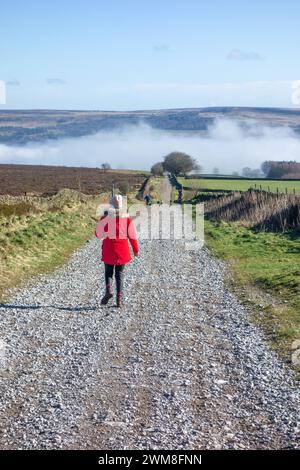 Frau im roten Mantel, die entlang der Sir William Hill Road läuft, einer alten Packhorse Route, die Teil des Sheffield to Buxton Turnpike Road Peak District war Stockfoto