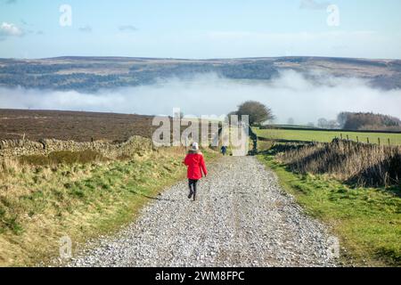 Frau im roten Mantel, die entlang der Sir William Hill Road läuft, einer alten Packhorse Route, die Teil des Sheffield to Buxton Turnpike Road Peak District war Stockfoto