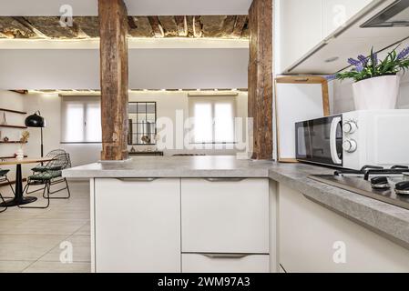 Eine Küche in einem Apartment mit zeitgenössischer Dekoration im industriellen Stil mit einer Servierluke zwischen antiken Holzsäulen Stockfoto