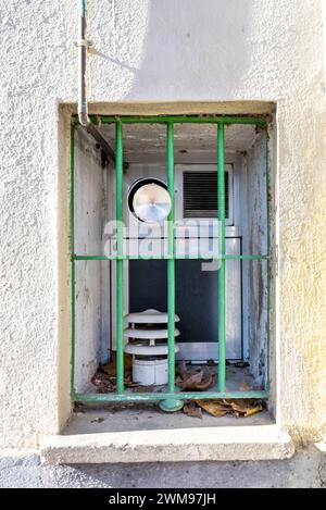 Ein kleines Fenster mit grünem Metallgitter und Rauchauslässen Stockfoto