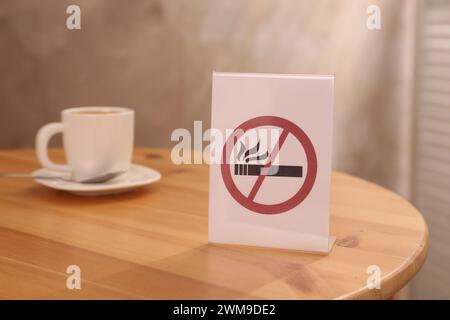 Rauchverbotsschild und eine Tasse Drink auf dem Holztisch drinnen, selektiver Fokus Stockfoto