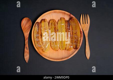 Gebratene Bananen mit geschmolzener Milch auf einem Holzteller. Beliebtes Street Food in Südostasien, besonders in Indonesien Stockfoto