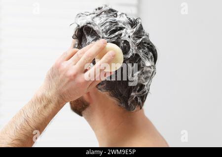 Mann wäscht sich die Haare mit einer festen Shampoo-Bar in der Dusche, Großaufnahme Stockfoto
