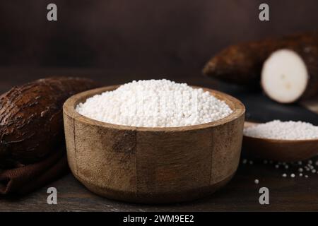 Tapioka-Perlen in Schüssel und Maniokwurzeln auf Holztisch, Nahaufnahme Stockfoto