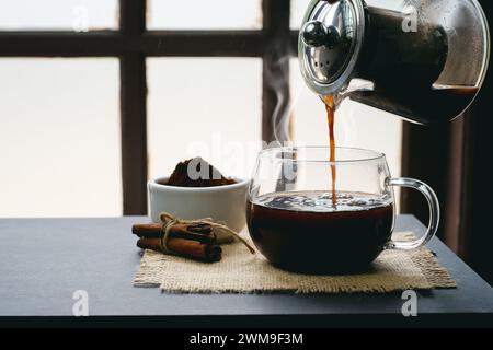 Zubereitung und Eingießen von heißem Kräuterkaffee in eine Tasse mit Dampf im Retro-Stil auf dem Tisch Stockfoto