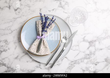 Besteck, Serviette, Teller, Glas und konservierte Lavendelblumen auf weißem Marmortisch, flache Ladefläche. Leerzeichen für Text Stockfoto