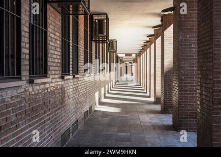 Durchgang im Erdgeschoss eines braunen Ziegelgebäudes mit Schatten der Säulen, Fluchtpunkt und Klimaanlagen in Metallkäfigen Stockfoto